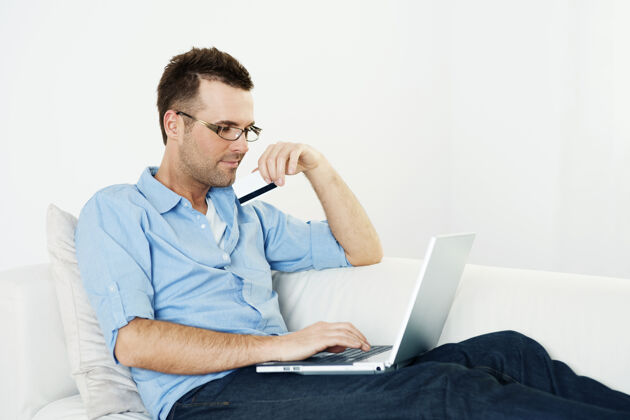 家庭金融在沙发上用信用卡和笔记本电脑的男人精益客户消费主义