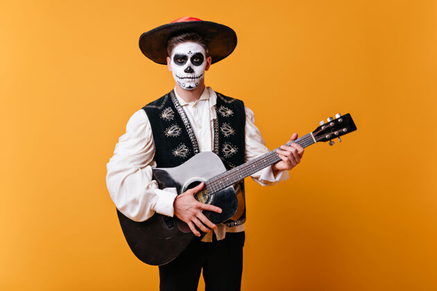 死亡帅气的马里亚奇站在黄色的墙上 带着僵尸的妆容万圣节的时候 一个穿着浓密睡衣的男人在弹吉他服装墨西哥歌手