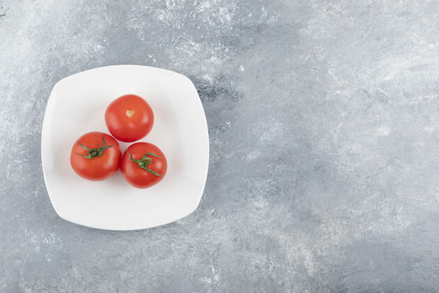 蔬菜在石头背景上放着三个新鲜的红色西红柿的白色盘子素食收获番茄叶子