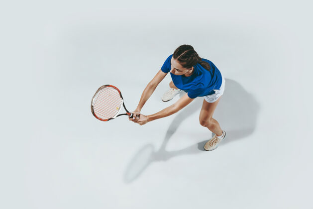 运动员穿蓝色球衣打网球的年轻女子她用球拍击球室内击球与白色隔离年轻 灵活 力量和活力负空间顶视图运动运动健康