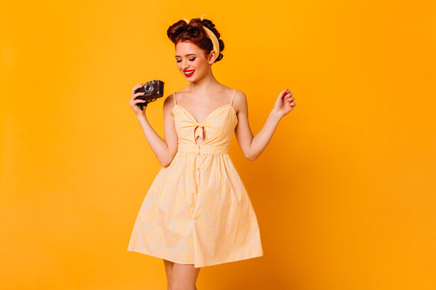 情感迷人的小女孩穿着裙子拿着相机摄影棚拍摄的微笑的女摄影师隔离在黄色的空间装束时尚积极
