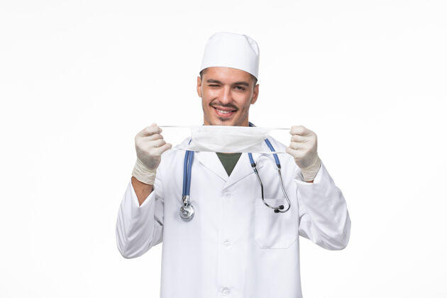 桌子正面图：男医生身着医疗服 戴着防冠状病毒口罩 白色办公桌上病毒冠状病毒-疾病大流行正面疾病人