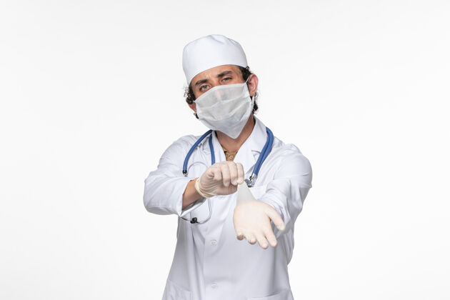 视图正面图男医生穿着医疗服 戴着无菌口罩作为防护罩 戴着白墙病毒手套就得了冠状病毒大流行病佩戴听诊器男性