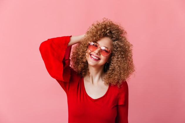 平衡一位穿着红色上衣的可爱女士看着镜头笑了起来这是一位戴着粉色眼镜的金发卷发女郎的照片表演女性表情