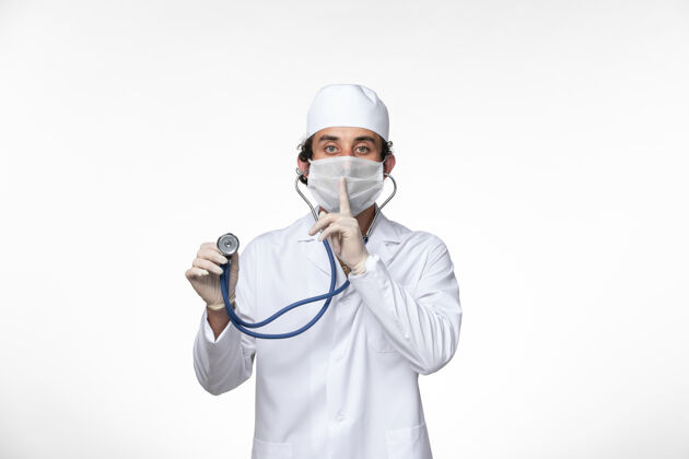 防护罩正面图：男医生穿着医疗服 戴着口罩以防病毒感染-使用听诊器对浅白壁病毒病进行病毒感染-大流行面罩医生覆盖