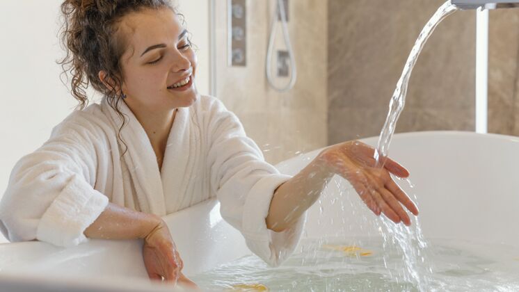 女人穿浴衣的女人把手放在水里房子浴缸浴袍