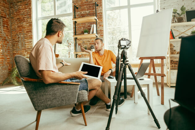 记录两位年轻的白人男性博主穿着休闲服 用专业设备或摄像机在家里录制视频采访视频日志大众现实