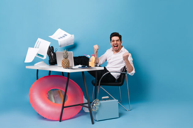官方一身办公装的男人在笔记本电脑里工作时 在一张掉落的纸中欢呼雀跃戴眼镜的男人拿着菠萝 手提箱和潜水面具摆姿势案件办公桌包