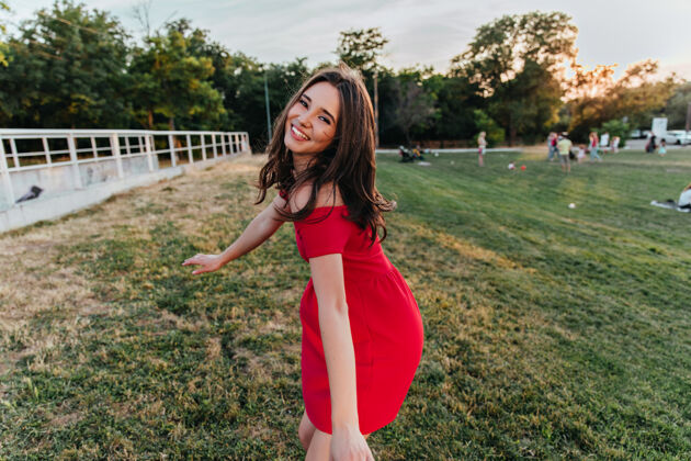 幸福优雅的黑发女孩表达着幸福美丽的黑发女人穿着红裙子在公园里玩的户外镜头花园放松户外