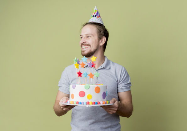 兴奋戴着节日帽的年轻人拿着生日蛋糕庆祝生日聚会快乐而兴奋地越过光墙光蛋糕庆祝