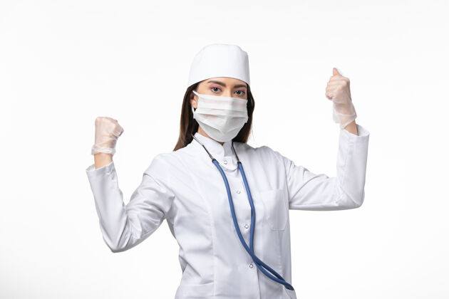 视图正面图女医生穿着白色无菌医疗服 戴着口罩 因柯维德-在白墙上战斗的姿势疾病柯维德-大流行病毒疾病医学女性面具