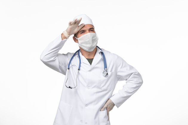 药物正面图：男医生穿着医疗服 戴着口罩 因为白色墙壁上的冠状病毒-医学大流行疾病套装外套医疗