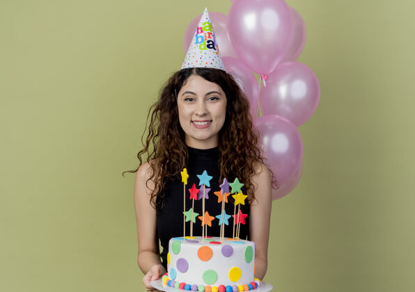 欢呼一个年轻漂亮的女人 卷发 戴着节日帽 手里拿着生日蛋糕 站在明亮的墙上 开心地笑着蛋糕卷发抱着