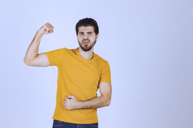 姿势穿黄衬衫的男人展示他的拳头和力量肌肉年轻聪明