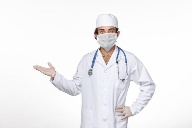 视图正面图男医生穿着医疗服戴着口罩在白墙上对抗冠状病毒大流行的药物面罩药大流行