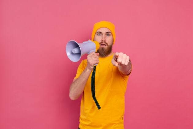 扩音器注意 一个拿着扩音器的欧洲男人用手指指着粉色背景上的相机演讲者肖像年轻人