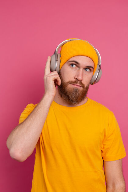 耳机帅哥在随意地听着音乐 用耳机隔离在粉色背景上享受歌曲使用