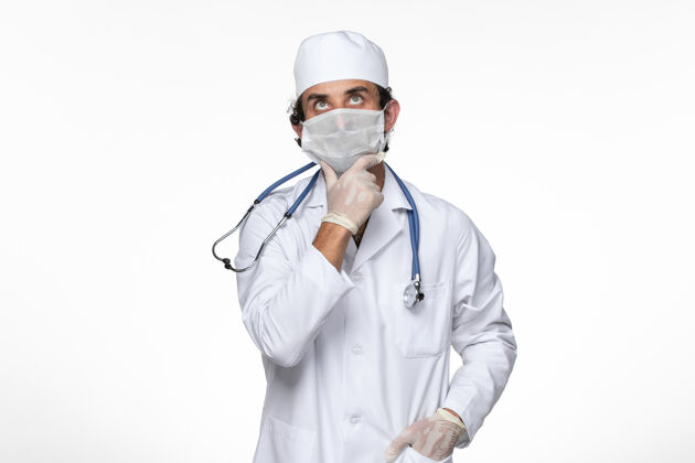 实验室外套正面图男医生穿着医疗服戴着无菌口罩以防病毒感染——思考白墙病毒病病毒的流行面罩思考消毒