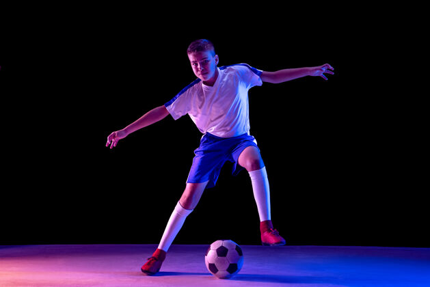 运动装小男孩像个足球运动员一样站在黑暗的墙上男孩游戏霓虹灯
