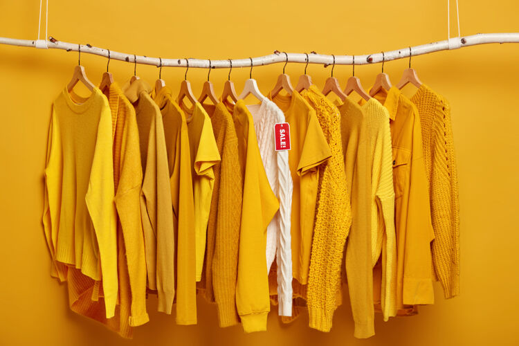 服装衣架上挂满了纯正的黄色女式毛衣一件白色毛衣脱颖而出 正在出售中时尚销售毛衣