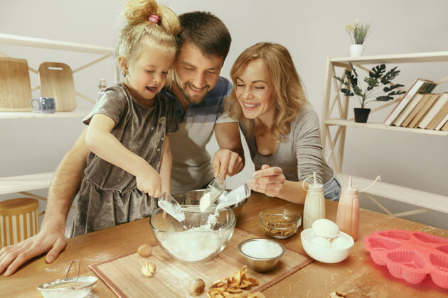 男性可爱的小女孩和她美丽的父母在家里的厨房里为蛋糕准备面团妈妈孩子健康