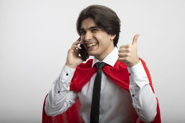 说话带着微笑的年轻超级英雄戴着领带在电话里讲话 在白色的地板上竖起大拇指超级英雄年轻电话