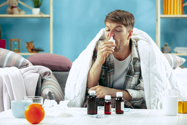 疾病留着胡须的病人坐在家里的沙发上 铺上暖和的毯子 用鼻喷雾剂对疾病 流感 疼痛有概念在家放松喷雾健康沙发