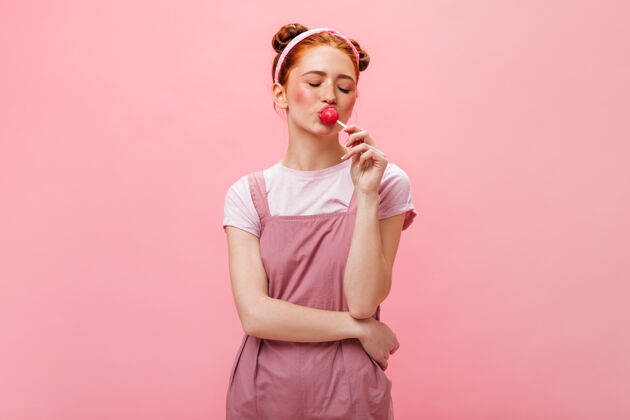 时尚一个穿着粉红色裙子的年轻女人 在孤立的背景下吃棒棒糖性感优雅头发