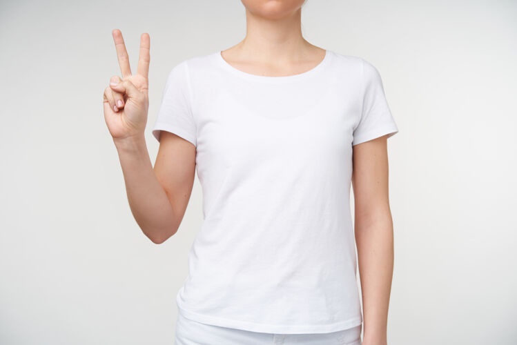 身体摄影棚的照片 年轻的女士显示两个手指 同时形成和平的姿态 用手语表示字母v 站在白色的背景白色提高女人