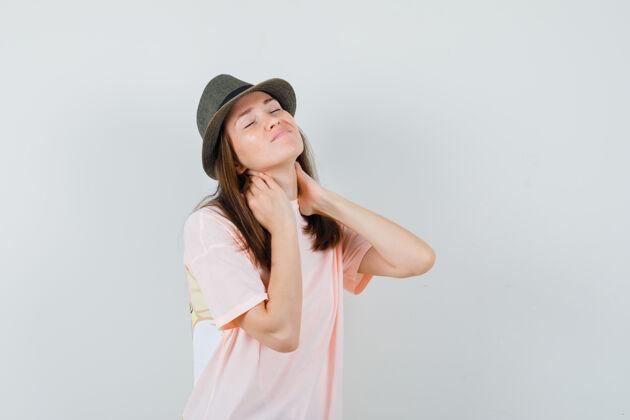 不舒服年轻女性患有颈部疼痛 穿着粉色t恤 戴着帽子 看上去不舒服 前视图年轻休闲女人