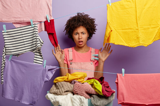 家务一个穿着工作服的愤怒的年轻女人和一个非洲裔女人摆姿势洗衣服房子晾衣绳休闲