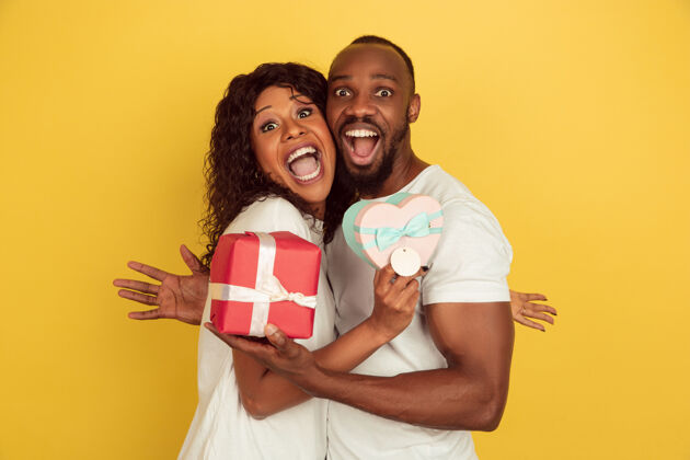 爱手持礼品盒情人节庆典 黄色工作室背景上的一对快乐的非洲裔美国夫妇情人面部表情