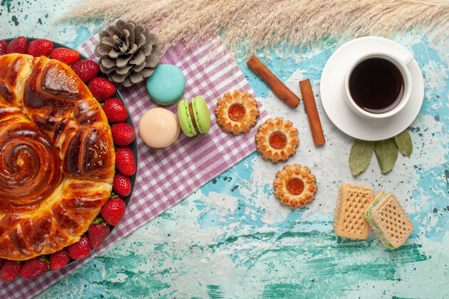 杯子俯瞰草莓派 配上饼干 法式马卡龙和蓝色表面的一杯茶盘子饼干食物