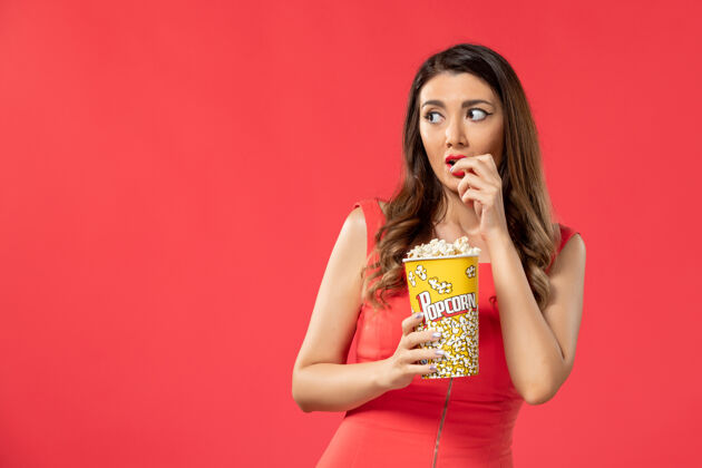 零食正面图穿红衬衫的年轻女性在吃爆米花 在红色的地面上看电影女性时间女士