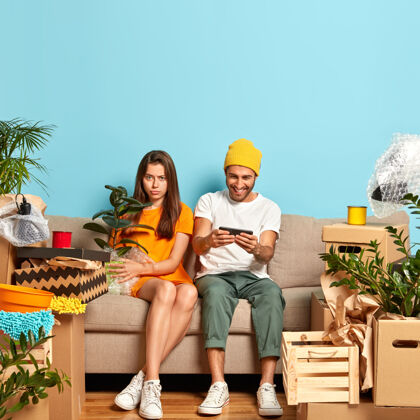 公寓一对悲伤的年轻夫妇坐在沙发上 四周都是盒子人壶植物