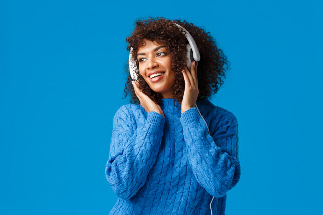 耳机性感迷人的非洲裔美国女性女孩 留着非洲式发型 穿着冬季毛衣 面带愉快的微笑 戴着耳机 听着歌手机欢乐礼物