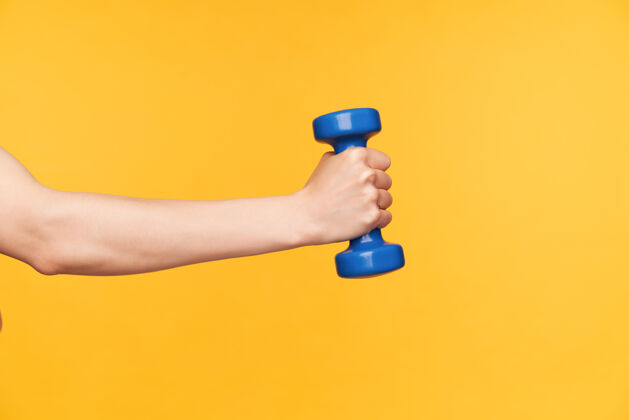 哑铃在黄色背景下 女性手举蓝色哑铃练习肱二头肌的侧视图身体护理和健身概念蓝色手指锻炼