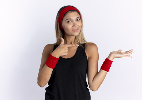 手指身穿黑色运动服 头戴红色头巾的年轻健身女孩 手指指向侧面 手臂站在白色墙壁上 呈现某种东西女孩手臂介绍