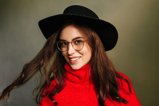 看戴着黑帽子 穿红毛衣的年轻女子 可爱的微笑 嬉戏着深色的头发楼梯聪明女孩