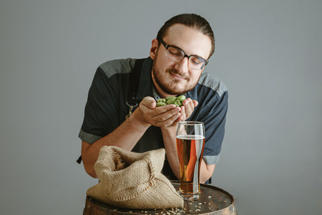 质量自信的年轻酿酒师 在灰色墙壁上的木桶上用玻璃瓶自制啤酒微型专业手臂