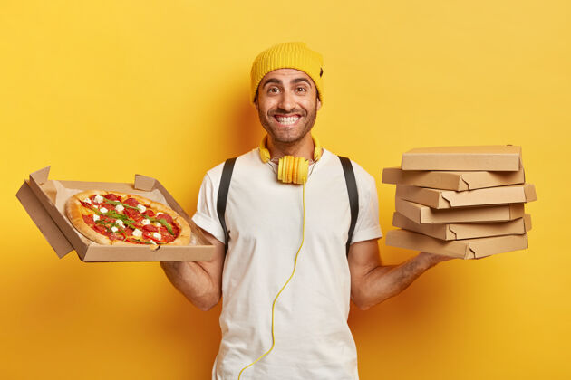 帽子面带微笑的漂亮送货员拿着披萨盒耳机举行男性