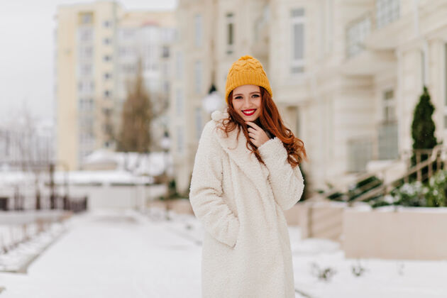 灵感美丽的白种人女孩在冬天的城市里散步穿着白大褂的姜黄色女人在街上摆姿势休闲寒冷寒冷的天气