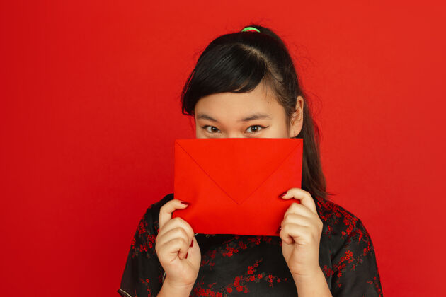 文案中国新年红色背景上孤立的亚洲少女肖像穿着传统服装的女模特看起来很梦幻 展示着红包庆祝 节日 情感服装女性微笑