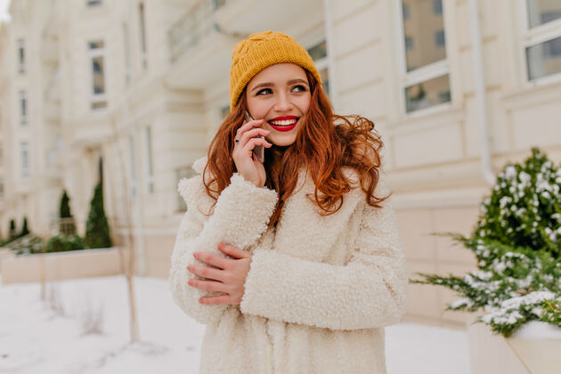 电话令人惊艳的红发女士微笑着和手机合影冬季早晨站在街上迷人的姜黄色女人的户外照片微笑姜雪
