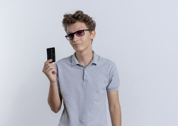 立场一个戴着黑眼镜 穿着灰色马球衫的年轻人站在白墙上 自信地展示着信用卡信心男人显示