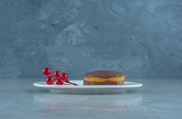 外套巧克力蛋糕和一簇圣诞浆果放在大理石背景的盘子上高质量的照片糕点美味烘焙
