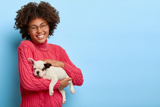 乐趣体贴的黑皮肤动物主人抱着小狗 喜欢宠物 戴着眼镜和粉色毛衣 开心地笑着空白粉色玩