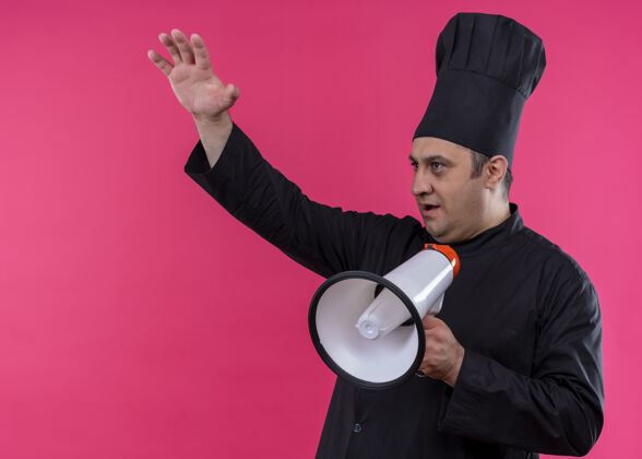 黑色男厨师身穿黑色制服 头戴厨师帽 对着扩音器高声喊叫 举起手 站在粉色背景下 向一旁张望穿站扩音器