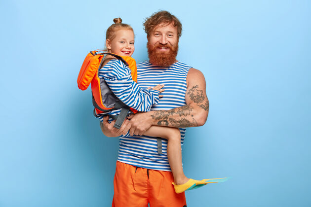 小快乐多情的爸爸手上抱着穿着救生衣和脚蹼的小女儿 一起去游泳 享受夏天的时光 留着姜黄色的头发红发一家在度假欢呼夏天夹克