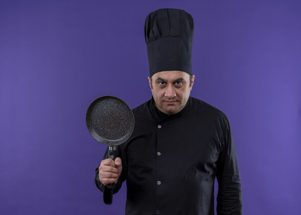 帽子男厨师身穿黑色制服 头戴厨师帽 手持煎锅 站在紫色背景下 表情严肃地看着镜头烹饪看着穿
